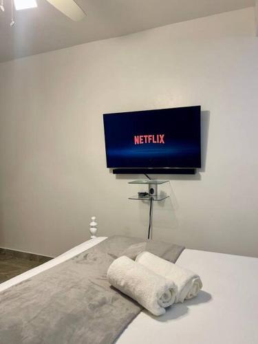 a television in a white room with towels on a bed at Super Cozy n´Confortable apart. in Ensanche Los Minas