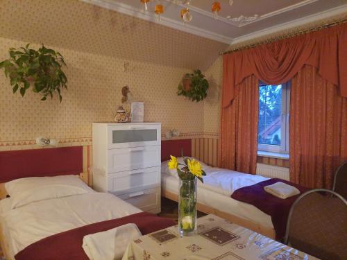 a bedroom with two beds and a table with a vase of flowers at Noclegi Sylana in Kobyłka