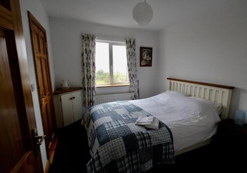 een slaapkamer met een bed met een deken en een raam bij Curlews Rest - Gateway to the Aran Islands in Galway