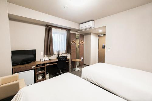 a hotel room with two beds and a desk at Smile Hotel Hakataekimae in Fukuoka