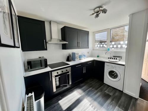 a kitchen with black cabinets and a washer and dryer at Lime Tree in blue Duplex Serviced Apartment in Cambridge