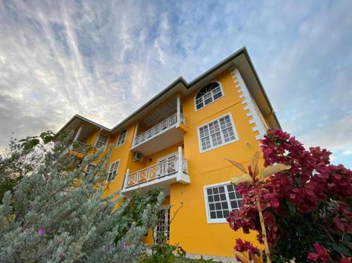 żółty budynek z białymi oknami i kwiatami w obiekcie Faith's Villa Tobago w mieście Diamond