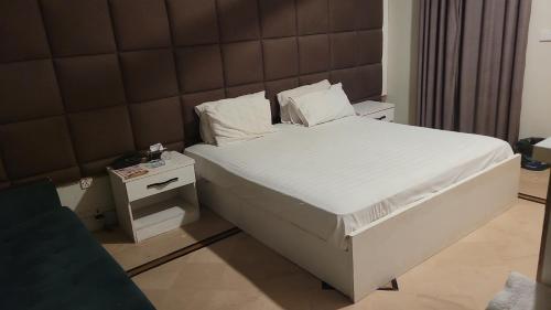 1 cama con sábanas blancas y almohadas en una habitación en Cottage Hotel, en Karachi