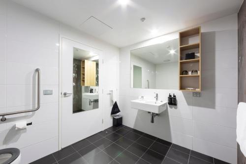 La salle de bains blanche est pourvue d'un lavabo et d'un miroir. dans l'établissement Avenue Hotel Canberra, à Canberra