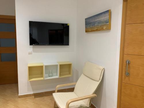 Pokój z białym krzesłem i telewizorem na ścianie w obiekcie Bonito y tranquilo apartamento en Nervión w Sewilli