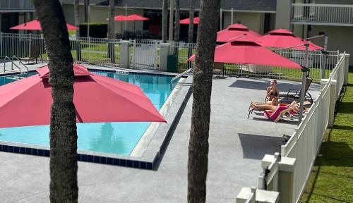 a pool with red umbrellas and a man sitting in a chair next to at Bposhtels Orlando Disney in Kissimmee