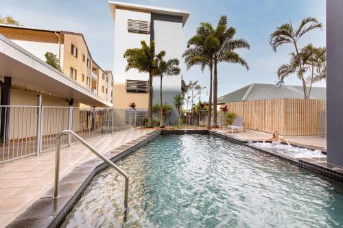 a swimming pool with palm trees and a building at Kings Beach Surf Retreat - Beautiful Views in Caloundra