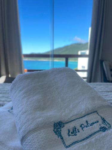 a stack of white towels on a bed with a window at Loft Pelicano Prainhas- Pontal do Atalaia- Para Casal - com Hidro in Arraial do Cabo