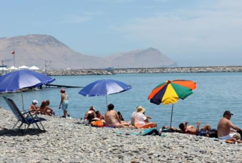 a group of people sitting on a beach with umbrellas at Modern Apartment close to the airport in Lima