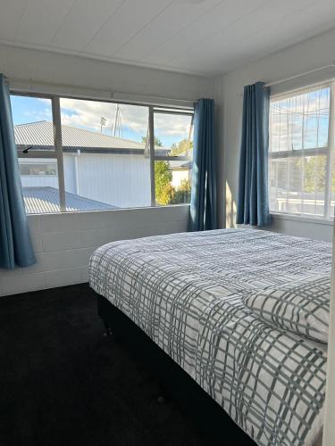 a bedroom with a bed with blue curtains and windows at Avon Apartments in Hamilton