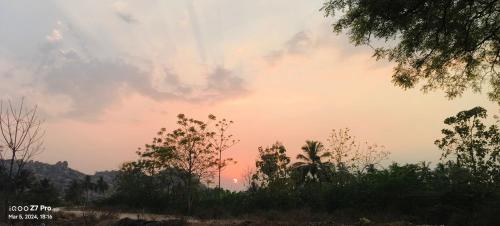 einen Sonnenuntergang am Himmel mit Bäumen im Vordergrund in der Unterkunft Leo home stay in Hampi