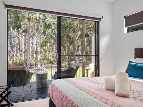 a bedroom with a bed and a balcony with trees at Tall Trees Margaret River in Margaret River Town