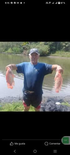 a man holding two fish in front of a body of water at Hotel y Hostal Mi Reino Represa Prado Tolima in Prado