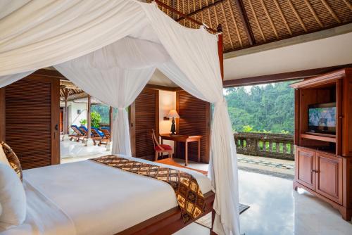 a bedroom with a canopy bed with a desk and a television at Puri Wulandari A Boutique Resort & Spa - CHSE Certified in Ubud