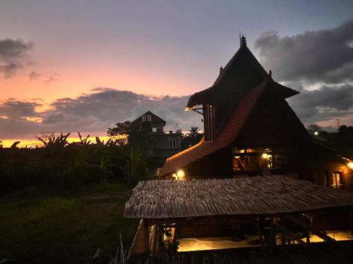 a house with a sunset in the background at Di Kubu YR in Jembrana