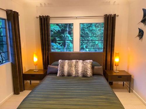a bedroom with a bed with two lamps and two windows at Aquatica - Luxe Holiday Home in Palm Cove