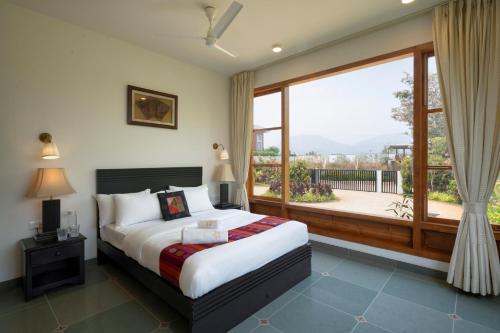 a bedroom with a bed and a large window at SaffronStays Niranta- 4-BDR villa on golf course near Bangalore in Bengaluru