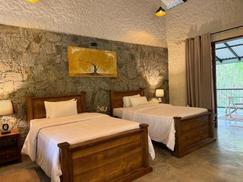 1 dormitorio con 2 camas y pared de piedra en Arsulana Eco Lodge & Spa, en Ginigathena