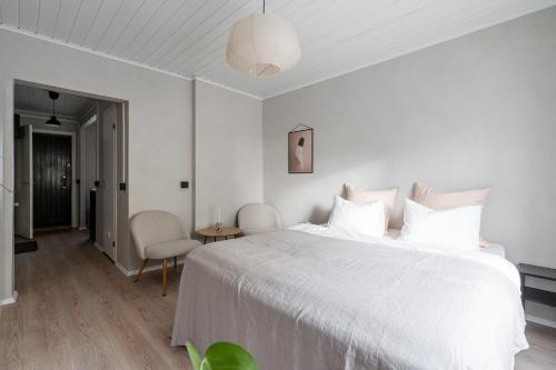a white bedroom with a large bed and a chair at Lovely Studio in Pispala in Tampere