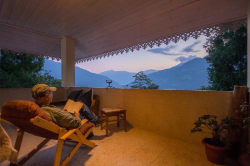 a man sitting in a chair on a porch with a laptop at La Ipsing Farm by StayVista, A heritage property in orchards with Mountain views, featuring Outdoor games and A cozy balcony for a memorable stay in Samdong