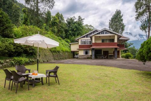 a table with an umbrella in front of a house at La Ipsing Farm by StayVista, A heritage property in orchards with Mountain views, featuring Outdoor games and A cozy balcony for a memorable stay in Samdong