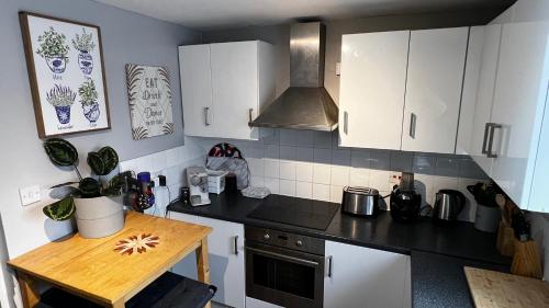 cocina con armarios blancos y encimera negra en Comfy apartment, en Londres