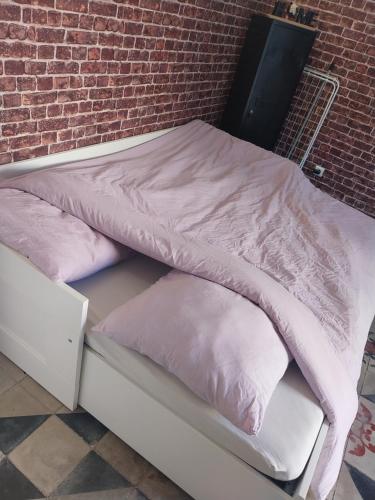 uma cama com lençóis e almofadas cor-de-rosa ao lado de uma parede de tijolos em Studio maillane em Maillane