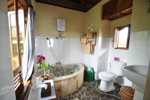 ein Badezimmer mit einer Badewanne, einem WC und einem Waschbecken in der Unterkunft Puri Lumbung Cottages Restaurant & Spa Munduk in Munduk