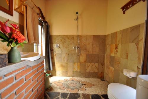 a bathroom with a shower and a toilet and a sink at Puri Lumbung Cottages Restaurant & Spa Munduk in Munduk
