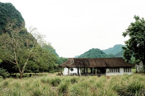 a building in a field with mountains in the background at Ancient House Cat Ba in Hai Phong