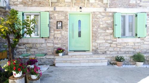 a stone house with green doors and windows and flowers at Captain Theo's modern apartment Maria in Lefkímmi
