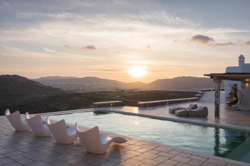 een zwembad met witte stoelen en de zonsondergang bij Mykonian Icon Villa in Mykonos-stad