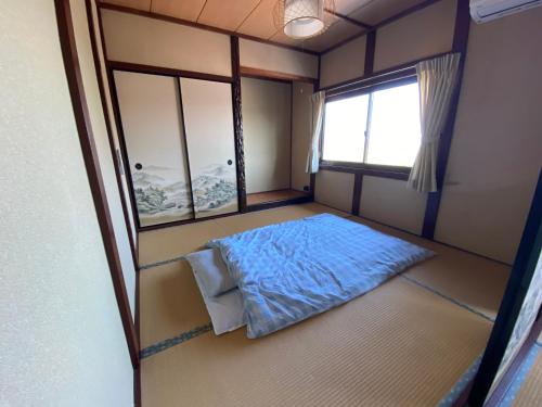 a small room with a bed and two windows at ゲストハウスすまいるさん in Iba