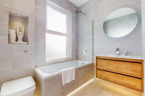 ein Badezimmer mit einer Badewanne, einem Waschbecken und einem Spiegel in der Unterkunft 5Bed Home w Free Parking & Garden - 8min to tube in London