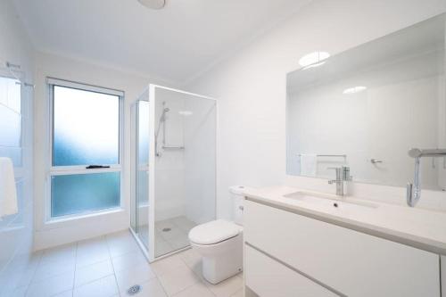 y baño blanco con aseo y ducha. en Water View Home - Minutes To Town, en Batemans Bay