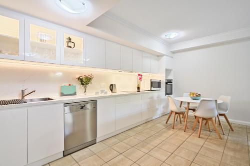 a kitchen with white cabinets and a table and chairs at Iluka Resort Apartments Palm Beach in Palm Beach