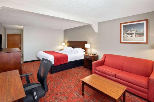 a hotel room with a bed and a red couch at Ramada by Wyndham Bowling Green in Bowling Green