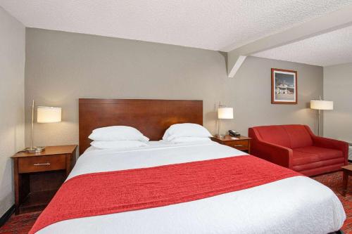 a hotel room with a bed and a red chair at Ramada by Wyndham Bowling Green in Bowling Green