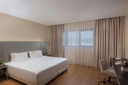 um quarto de hotel com uma grande cama branca e uma secretária em NH Orio Al Serio em Orio al Serio