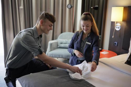 a man and a woman preparing a bed in a hotel room at Holiday Inn Lübeck by IHG in Lübeck