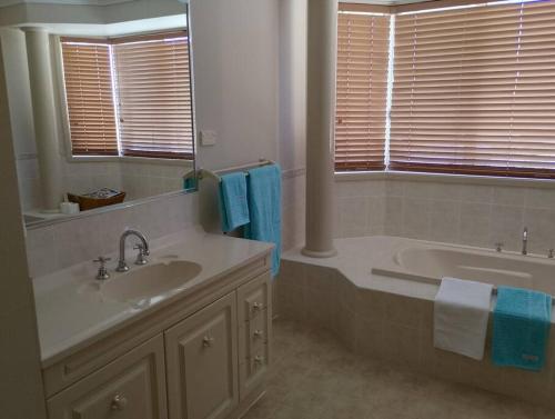 ein Badezimmer mit einem Waschbecken, einer Badewanne und einem Spiegel in der Unterkunft Mansion @ the Coast in Albion Park