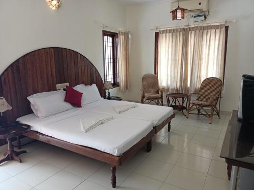 a bedroom with a bed and chairs and a television at The Bunglow in Kovalam
