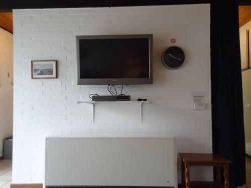 a tv on a white brick wall with a clock at Bungalow 5566 in Tossens in Butjadingen OT Tossens