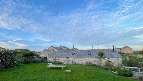 a stone house with a bench in the yard at Trengothal Barn in Porthcurno