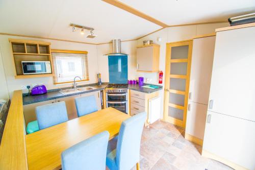 a kitchen with a wooden table and blue chairs at MP639 - Camber Sands Holiday Park - 3 Bedroom - Sleeps 8 - Large gated decking - Close to facilities in Camber