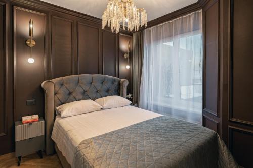 1 dormitorio con 1 cama con lámpara de araña y ventana en The Episode - Jacuzzi Penthouses en Cluj-Napoca