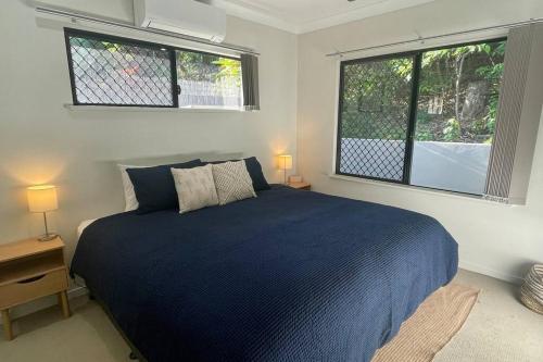 a bedroom with a blue bed and two windows at New Pool Now Open! - Trinity Beach Haven - Luxury 4 bedroom home, Steps to the Beach, Surrounded by Mountains in Trinity Beach
