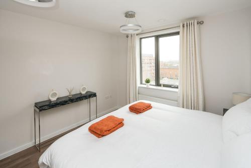 1 dormitorio con 1 cama blanca y 2 toallas de color naranja en Canning town -2 bed Luxury Apartment, en Londres