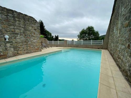 une grande piscine bleue à côté d'un mur en pierre dans l'établissement Maison avec piscine - Juvinas, à Juvinas