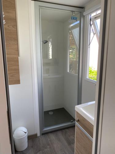 een douche in de badkamer met een wastafel en een spiegel bij Mobil home 8 personnes in Lattes
